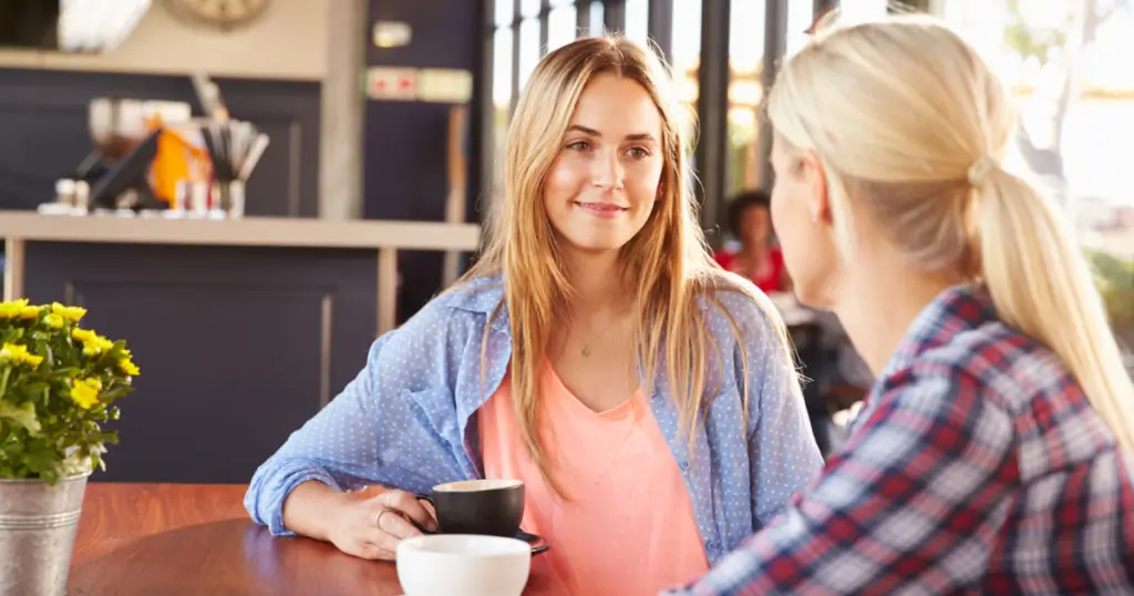 Two women having a calm and friendly conversation over coffee in a cozy café, illustrating the concept of setting boundaries in a positive way.