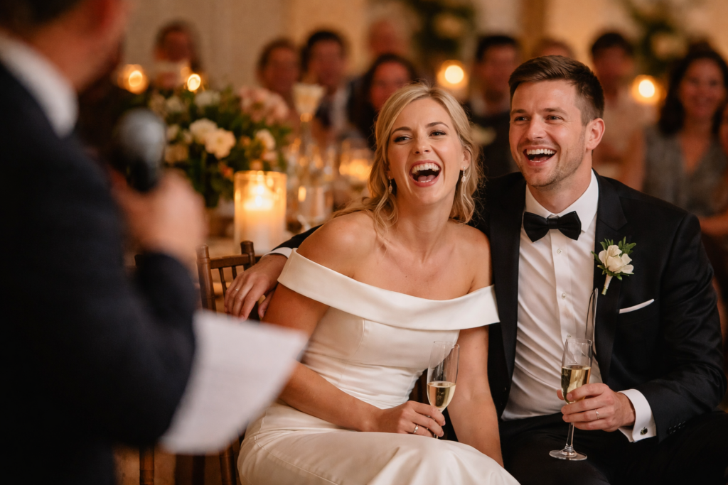 Bride and groom laughing during a wedding reception as guests enjoy a joyful, personal celebration